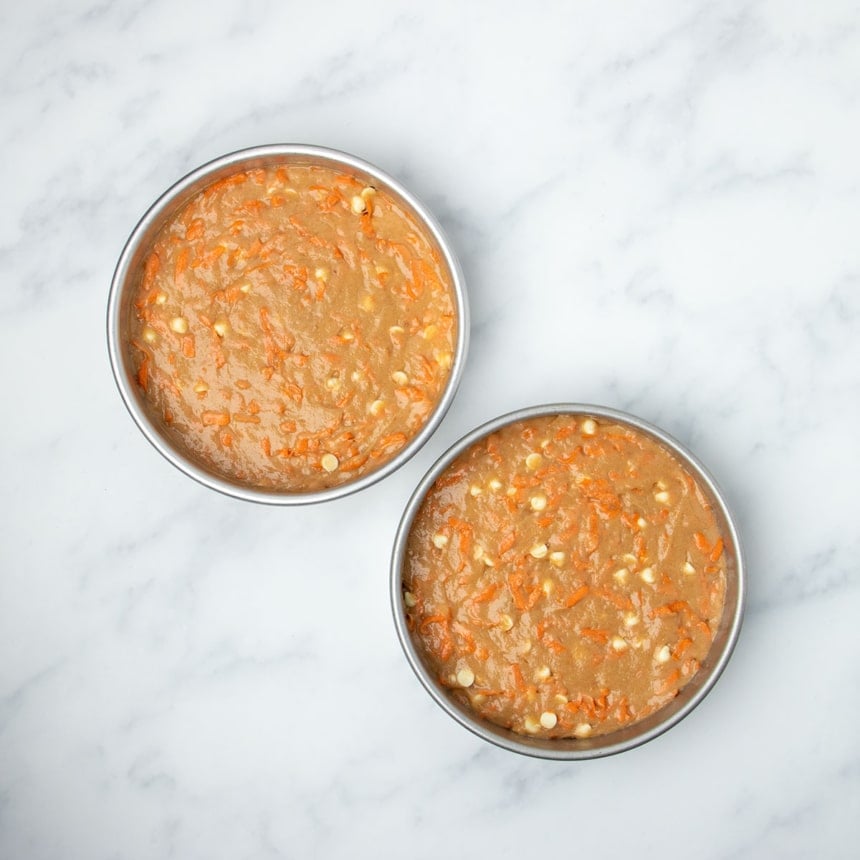 two round 8-inch metal cake pans with wet raw gluten free carrot cake batter with visible carrot shreds and white chocolate chips