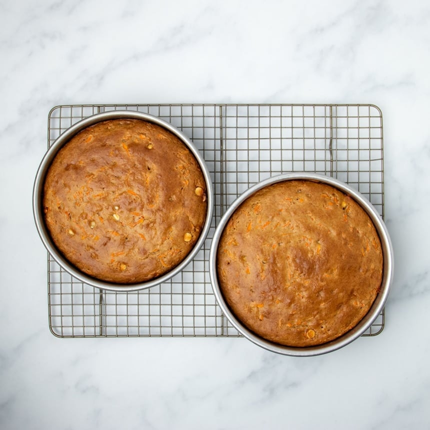 same 2 round cake pans with baked browned carrot cake on wire rack