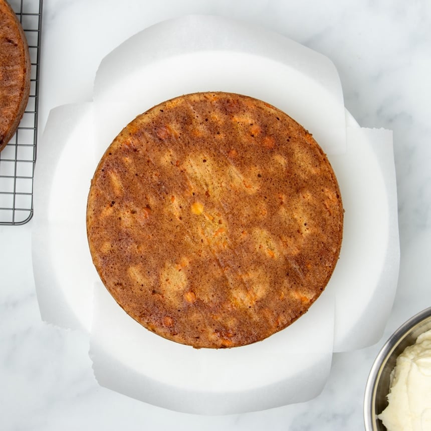 one round light brown carrot cake overturned on four strips of white parchment paper