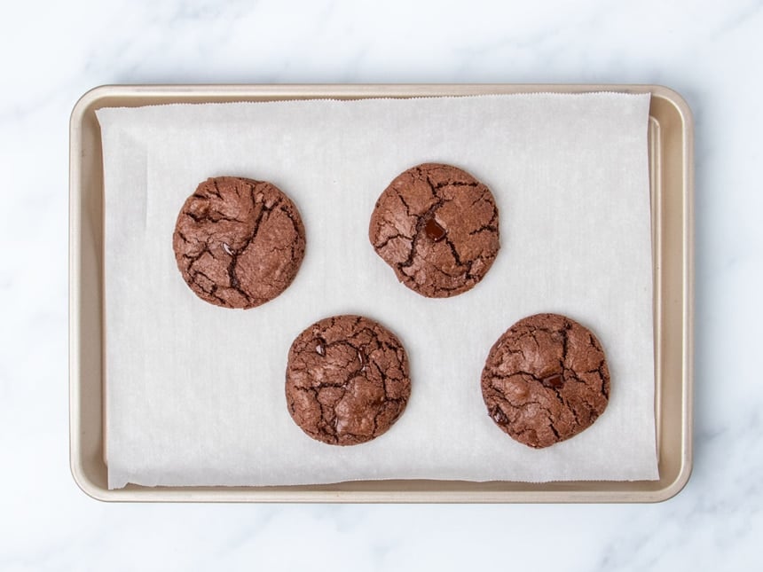 4 baked chocolate cookies spaced evenly apart on white paper on gold tray