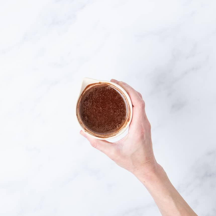 hand holding brown melted chocolate and butter mixture in small light tan ceramic bowl