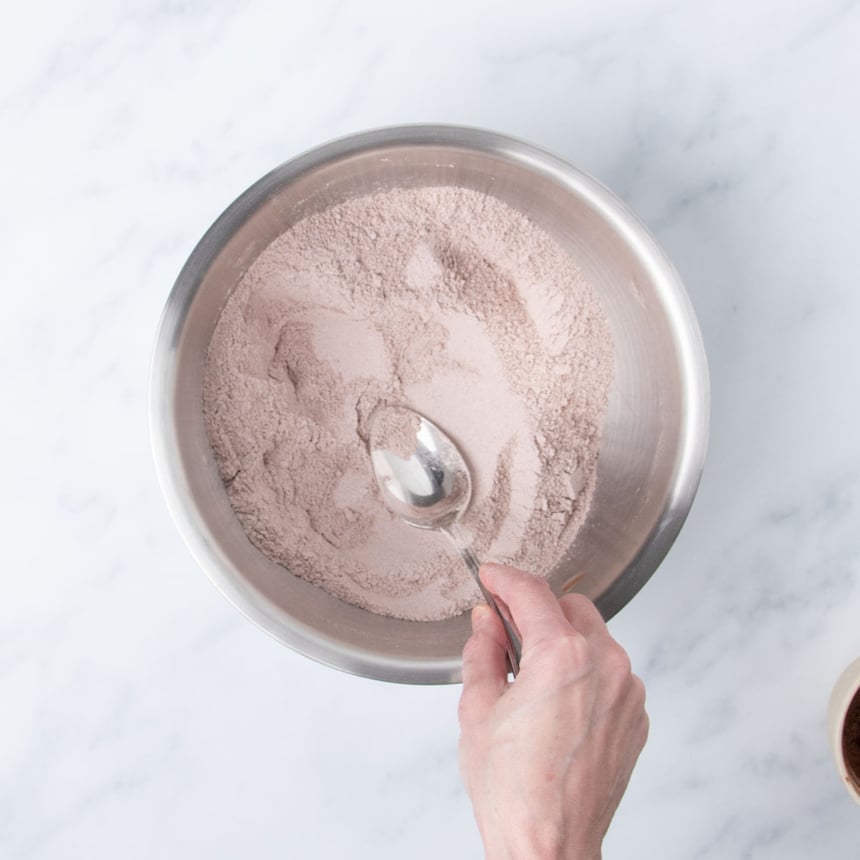 hand holding mixing spoon pressing down into light brown powder in bowl