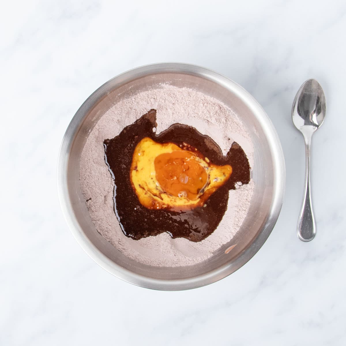 brown liquid melted chocolate with beaten eggs and light brown vanilla on pale brown powder in bowl