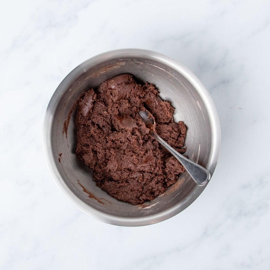 thick dark brown unshaped cookie dough with metal mixing spoon in bowl