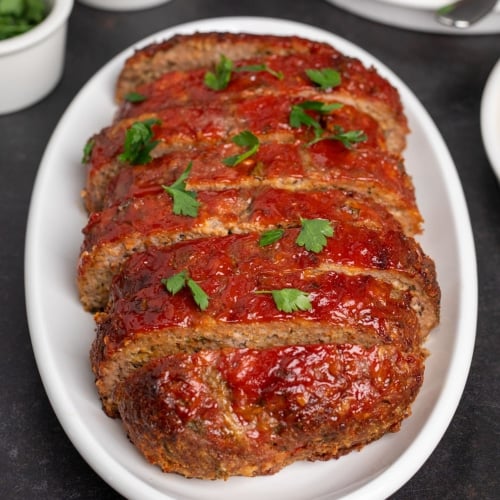 slices of gluten free meatloaf on oval white platter with scattered parsley