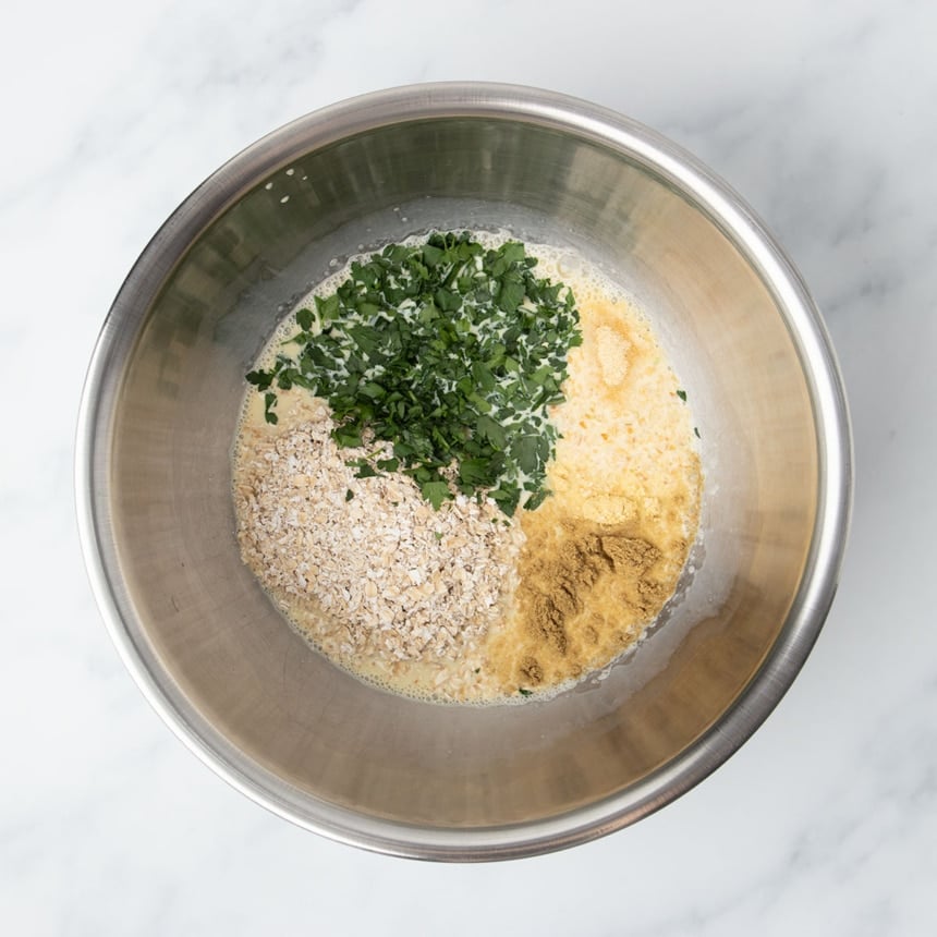 Light yellow and brown ground spices, chopped green fresh parsley, and quick oats on top in same mixing bowl