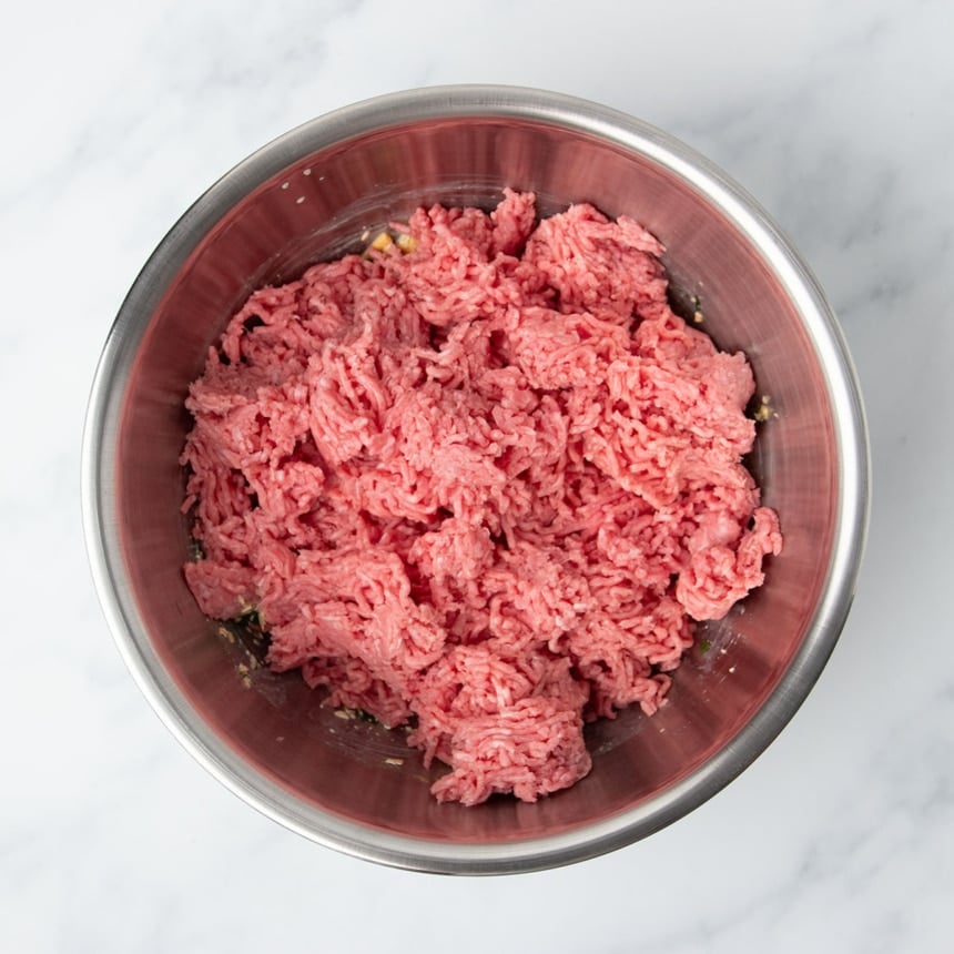 light red ground beef on top of other ingredients in bowl