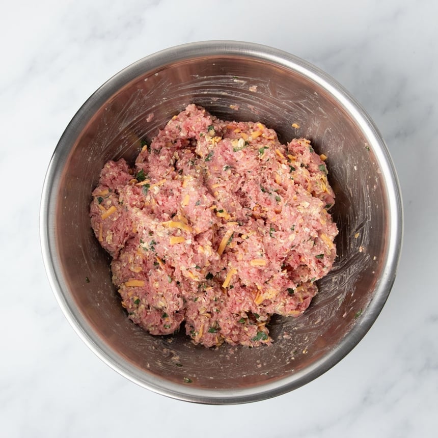 mixed meatloaf mixture with red beef, green parsley leaves, yellow cheddar in bowl