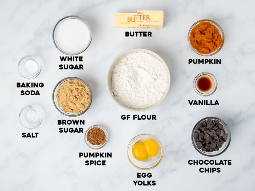 ingredients for gluten free pumpkin chocolate chip cookies in small bowls with names of ingredients below each bowl on light marbled surface