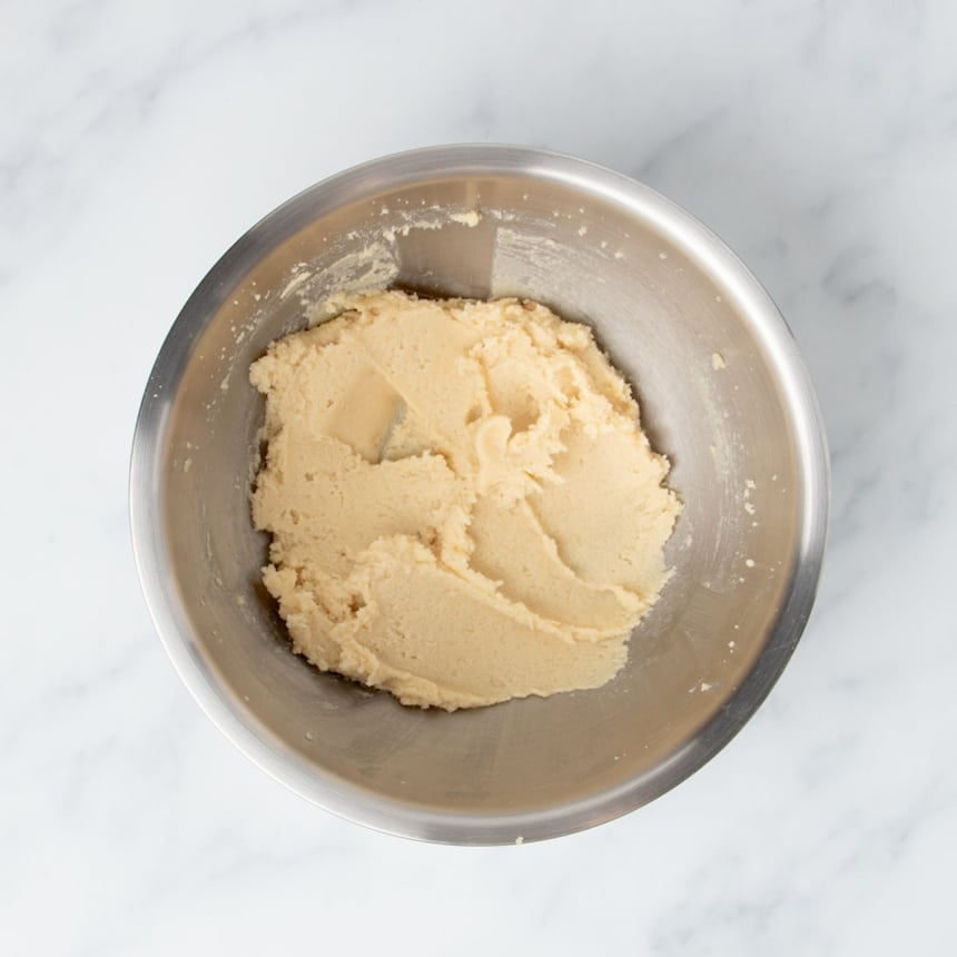 Large round metal mixing bowl with soft and fluffy light brown mixture of brown sugar, white sugar and butter