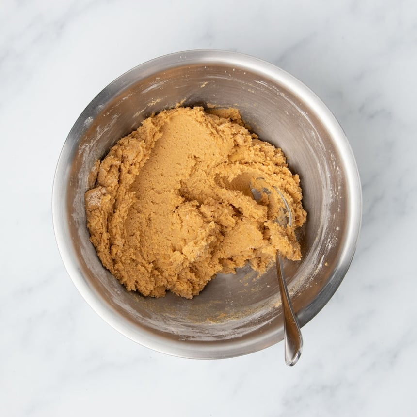 All dry ingredients mixed into wet in same mixing bowl with large metal mixing spoon into thick light orange cookie dough