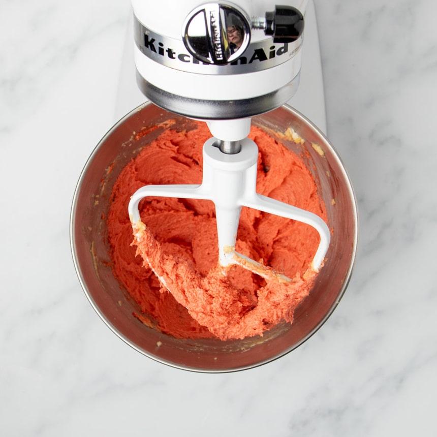 light red butter and sugar batter in bowl and on white flat mixer paddle