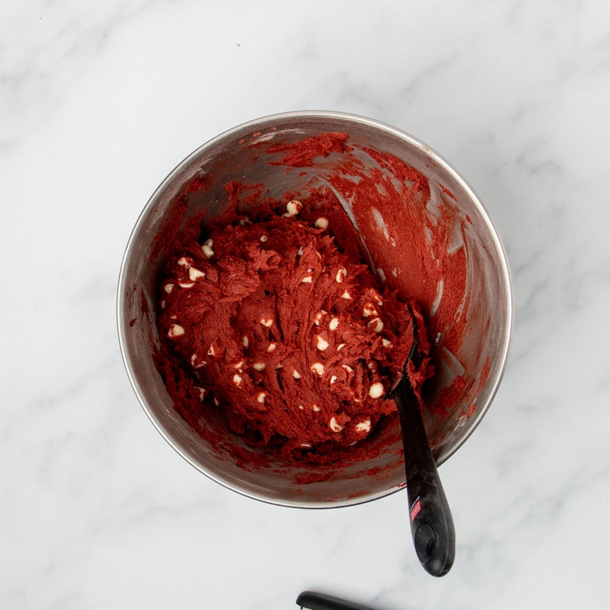 red velvet cookie dough with white chocolate chips in mixing bowl with black silicone spatula handle