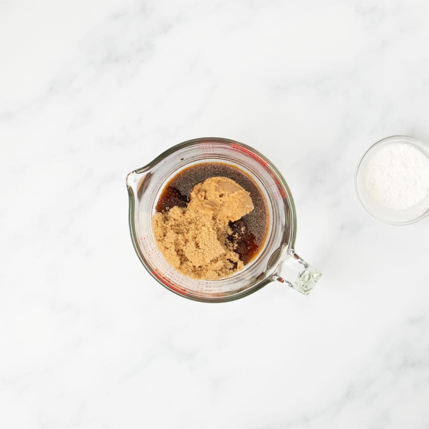 2 cup pyrex measuring cup with brown liquid, powdered spices, and brown sugar