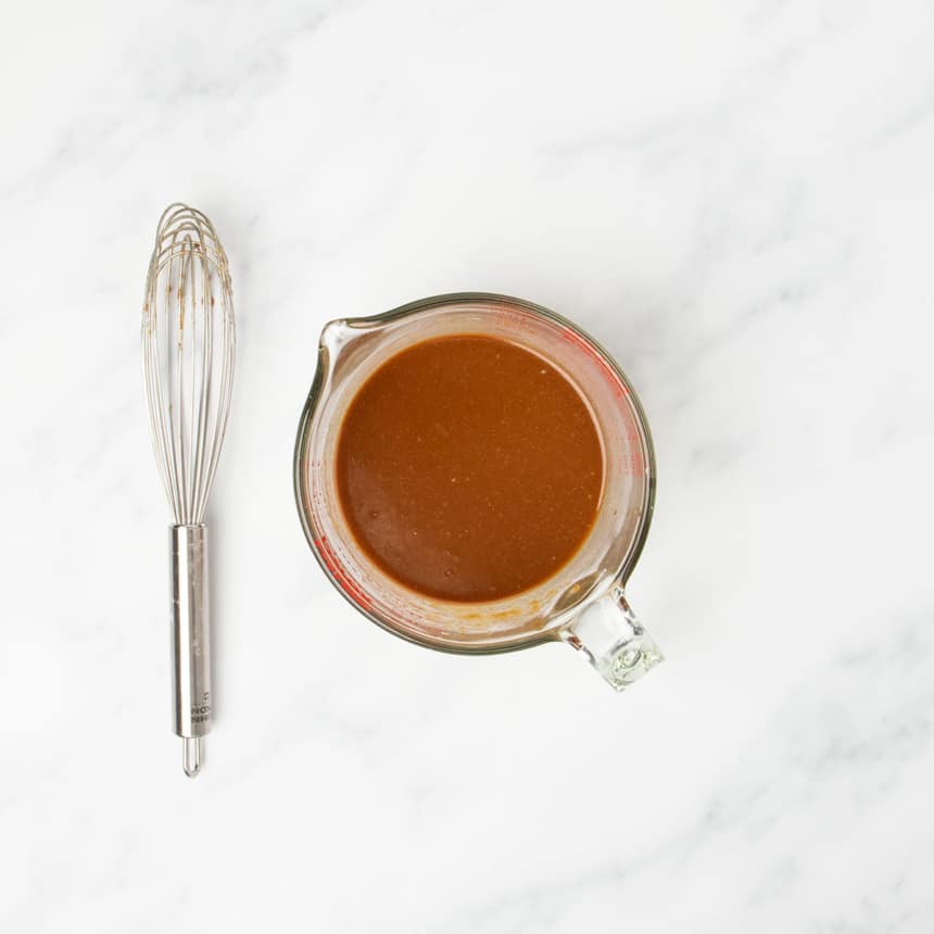 lighter brown liquid gluten free stir fry sauce whisked together in measuring cup with whisk on side