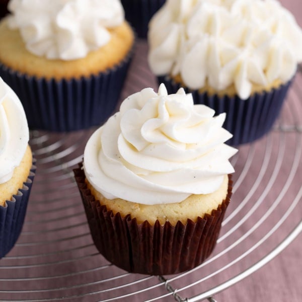 gluten free vanilla cupcake in brown wrapper with white frosting on round wire rack