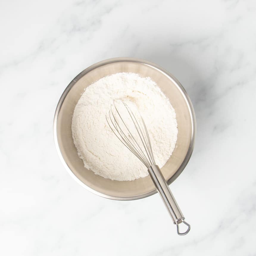 small round metal mixing bowl with whisked white powder and wire whisk