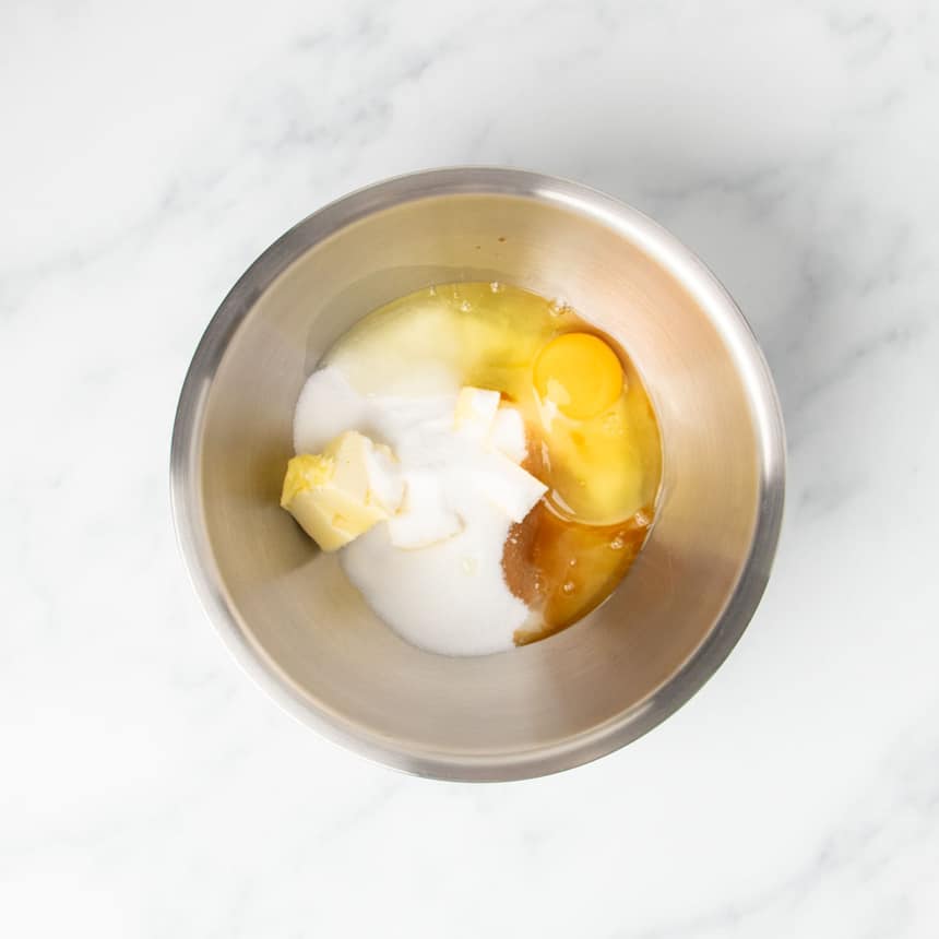 large round metal mixing bowl with butter, white sugar, vanilla, and egg