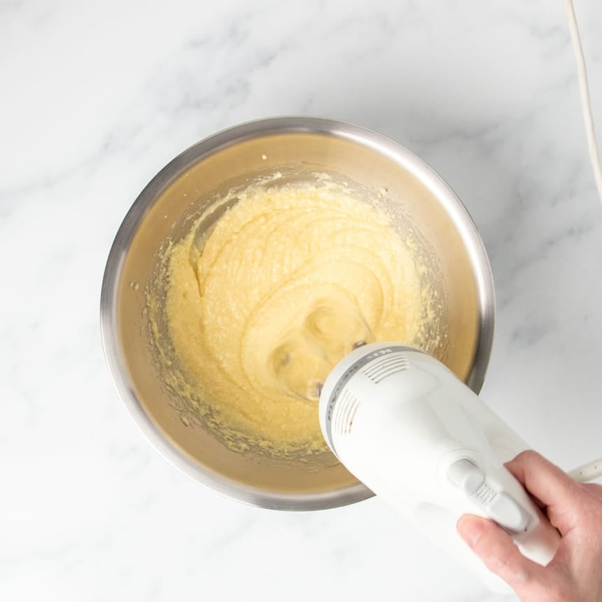 white handheld mixer beating light yellow mixture in same mixing bowl