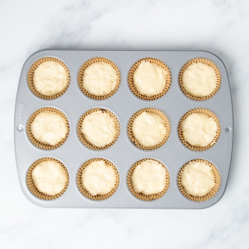 standard 12 cup metal muffin tin with brown muffin liners in wells filled 2/3 of the way full with light yellow raw cupcake batter