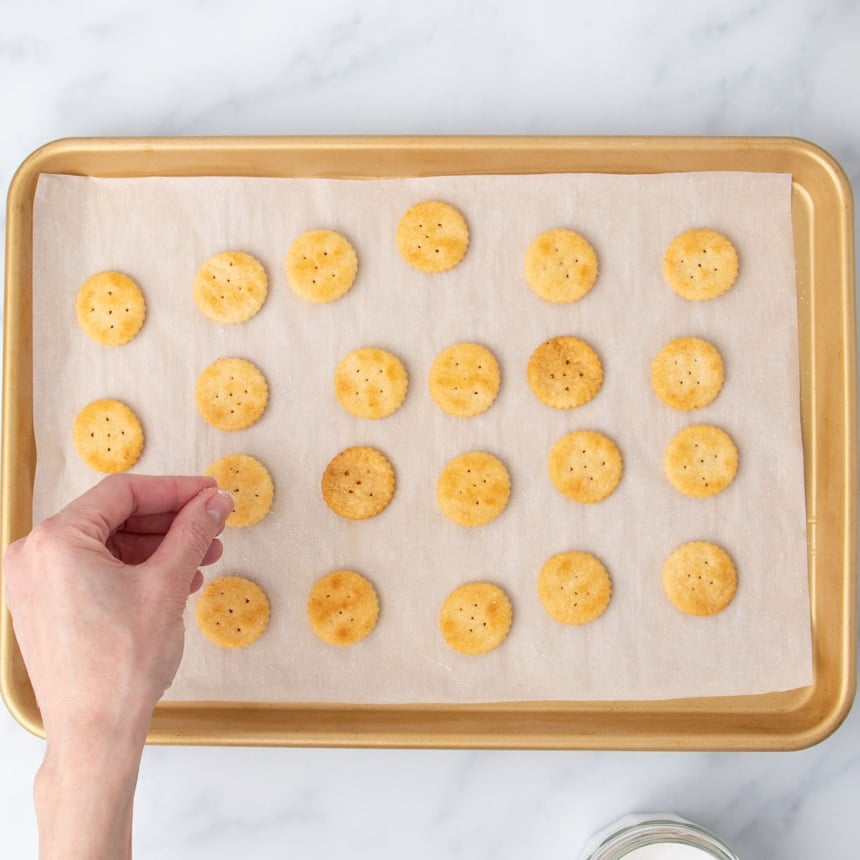 hand sprinkling white kosher salt on same crackers on baking tray