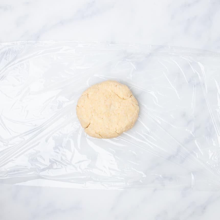 flat semi-round disk of cracker dough on plastic wrap on marble surface