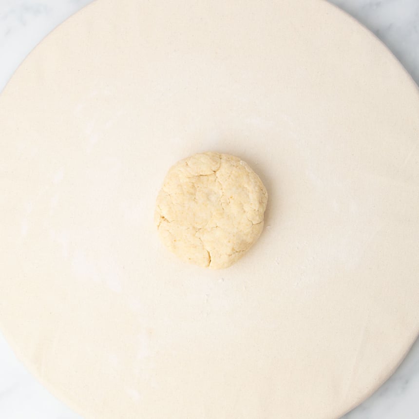 unwrapped disk of dough on tan fabric on round pastry board