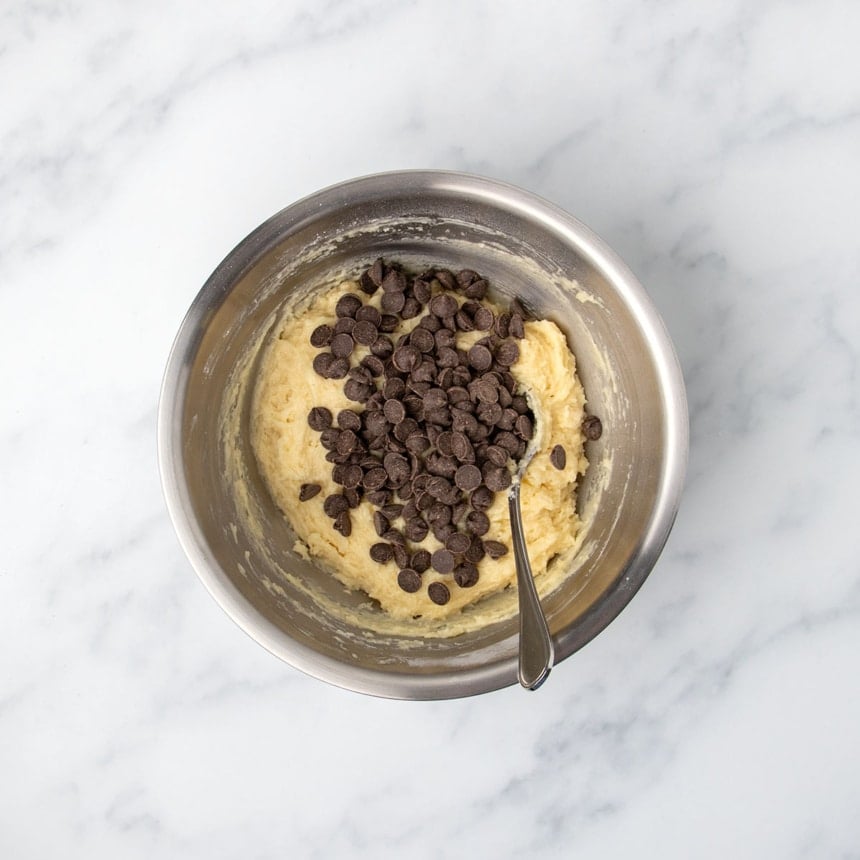 mixed thick light yellow muffin batter with chocolate chips on top and large metal mixing spoon