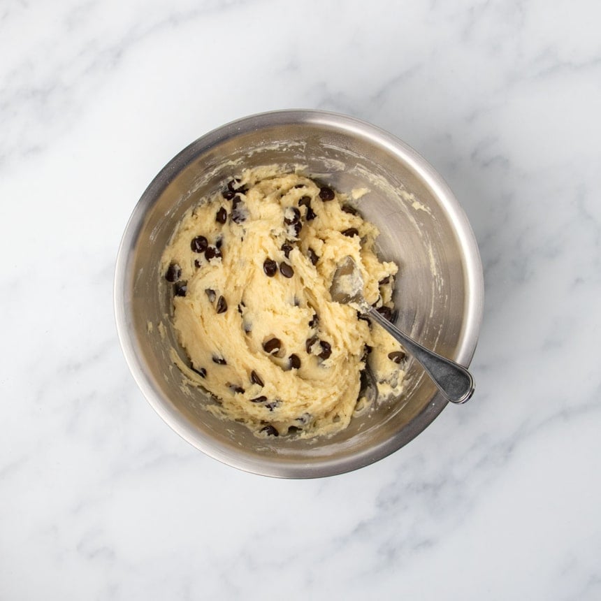 raw prepared light yellow gluten free muffin batter with chocolate chips mixed in and metal mixing spoon