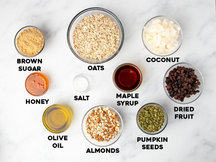 overhead image of ingredients to make gluten free granola in small round glass bowls with names of ingredients in black bold type