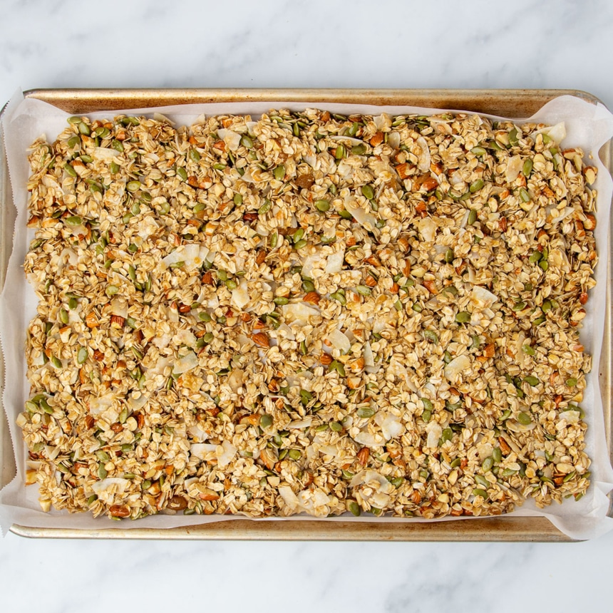 Raw granola mixture from bowl now on large rectangular metal half sheet pan lined with paper