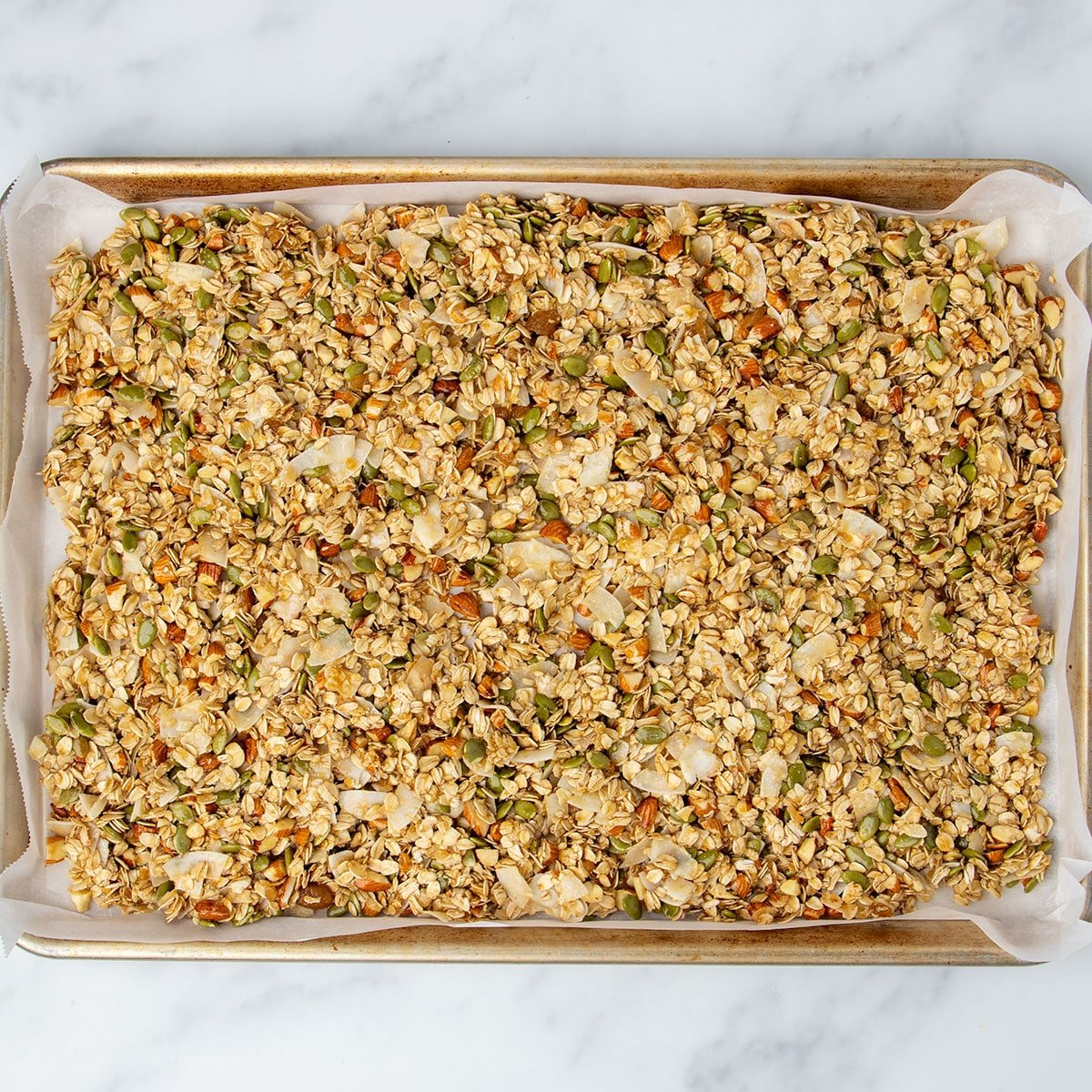Raw granola mixture from bowl now on large rectangular metal half sheet pan lined with paper