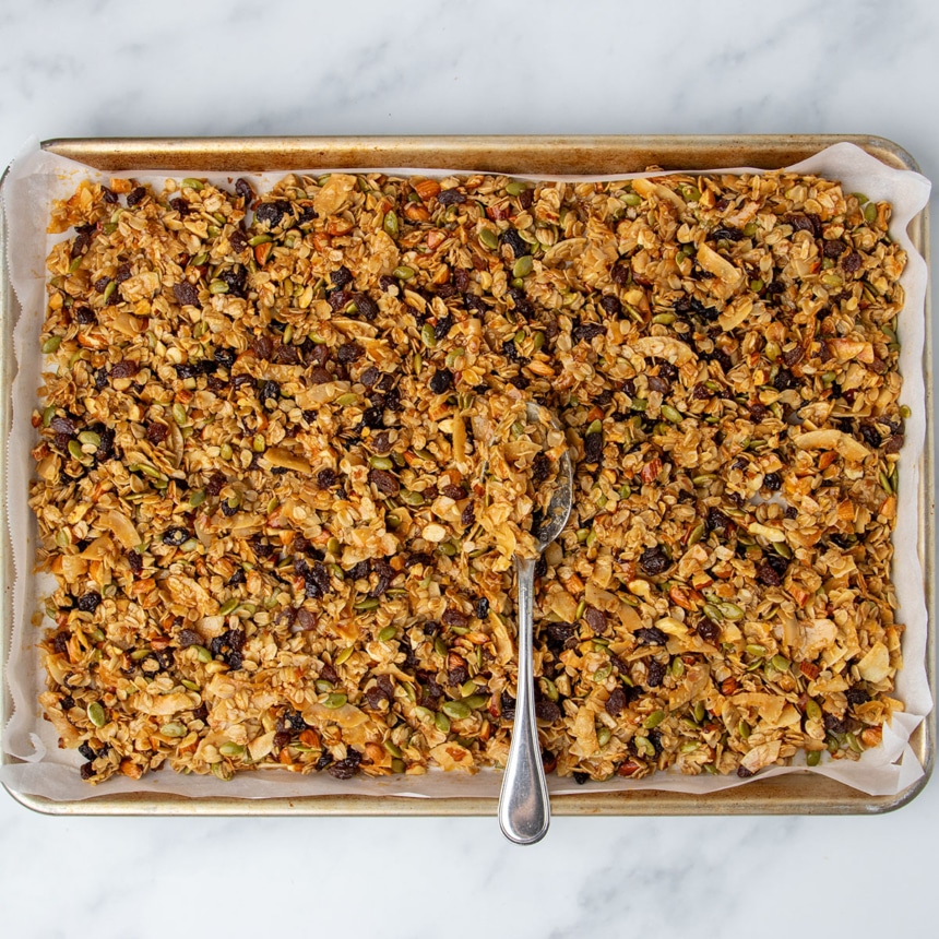 fully baked mixture with dark brown and black raisins mixed in throughout granola, cooling in single layer on baking sheet