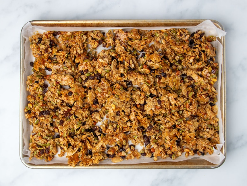 granola mixture still on baking sheet, but broken up into large chunks with melted brown glaze on bottom of some chunks