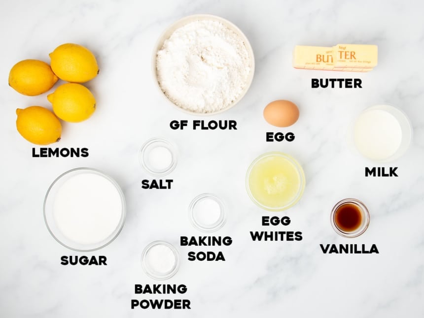 ingredients for gluten free lemon cake on marble surface, most ingredients in small glass bowls with black type for names of ingredients