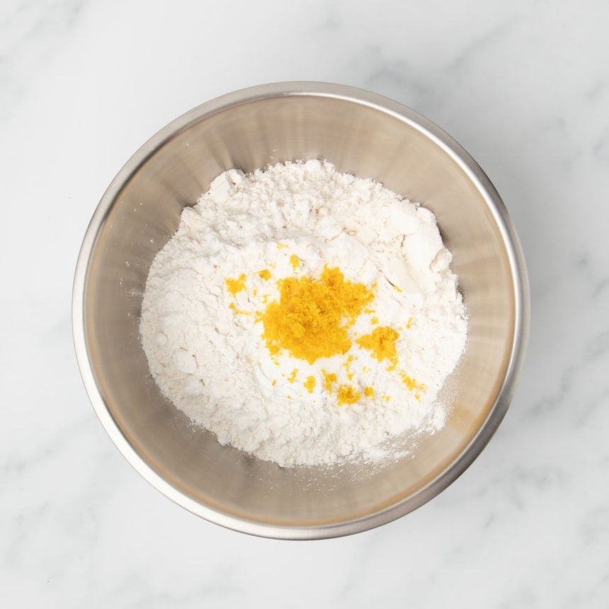 Medium size metal round mixing bowl with white powders and yellow lemon zest