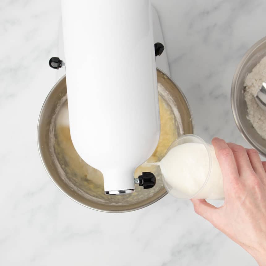 hand pouring milk into mixer bowl while it's beating