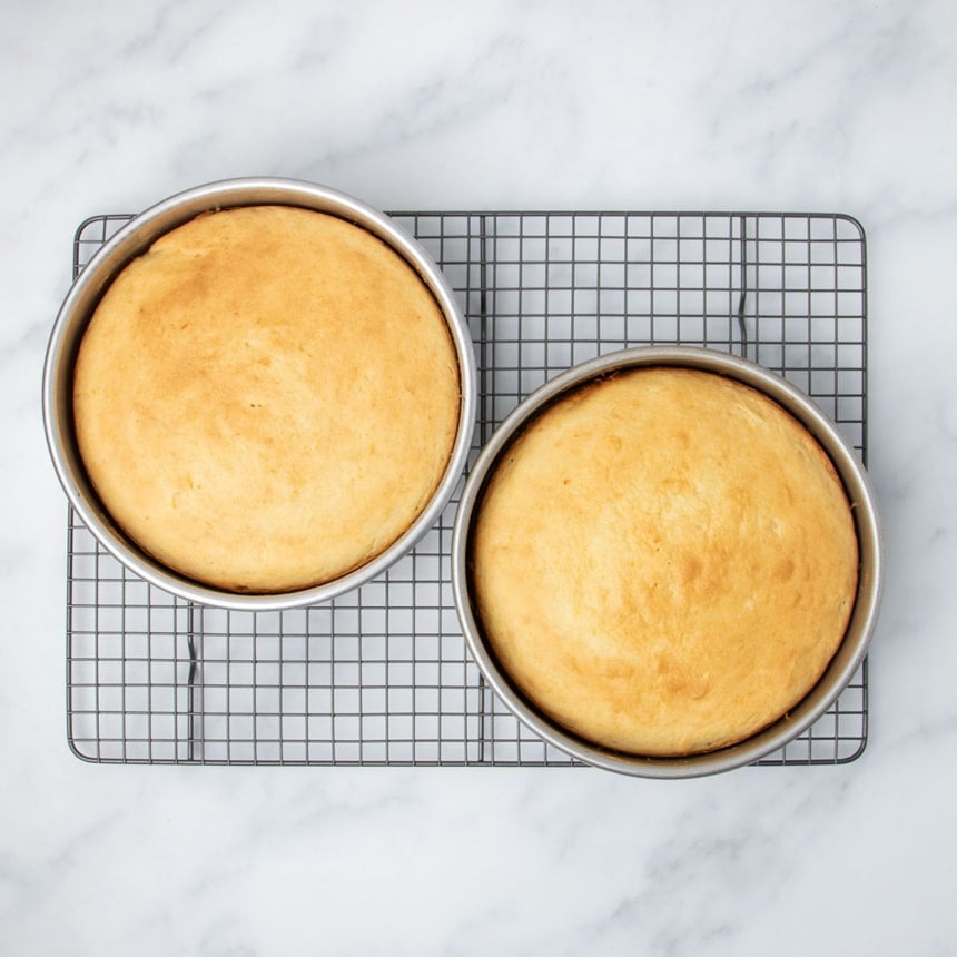 baked yellow cakes that are also baked light brown in spots on top, both on dark metal wire cooling rack