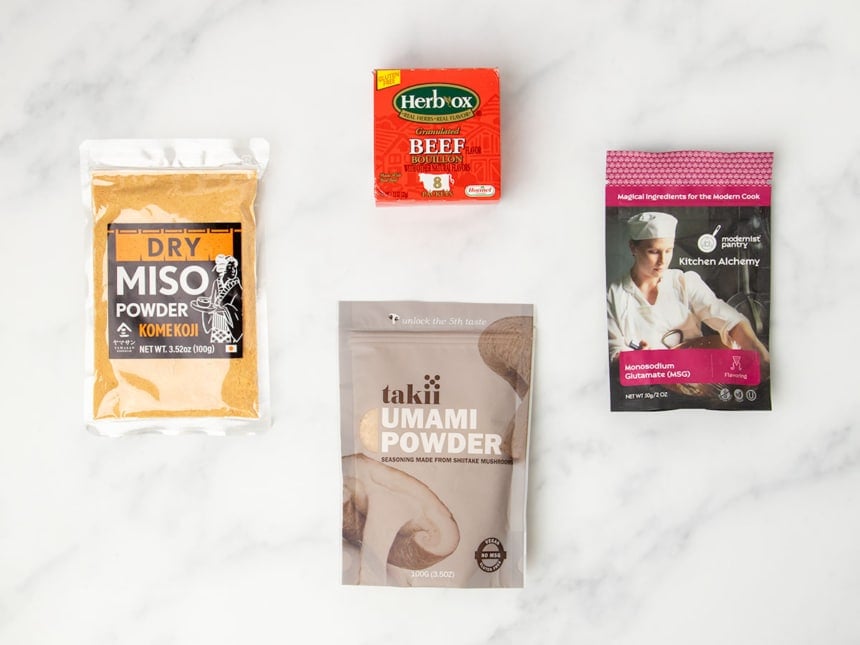 overhead image of red box of HerbOx brand beef bouillon, pouch of yellow dry miso powder Komekoji brand, Takii Umami powder brown pouch, Kitchen Alchemy brand pouch of Monosodium Glutamate (MSG)