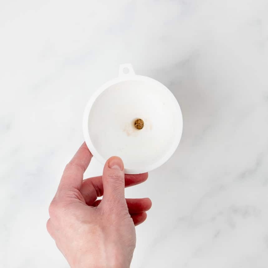 hand holding small white funnel used to transfer dry onion soup mix ingredients into small glass container