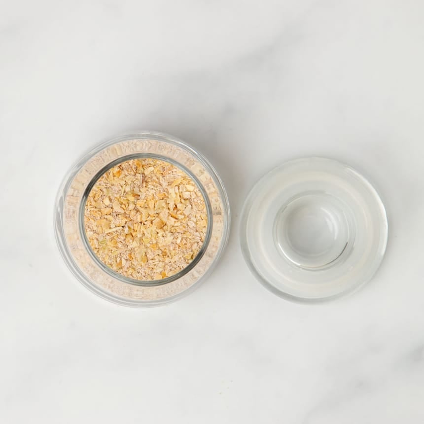 light yellow dry onion soup mix in small open glass jar with top next to the jar on marble surface