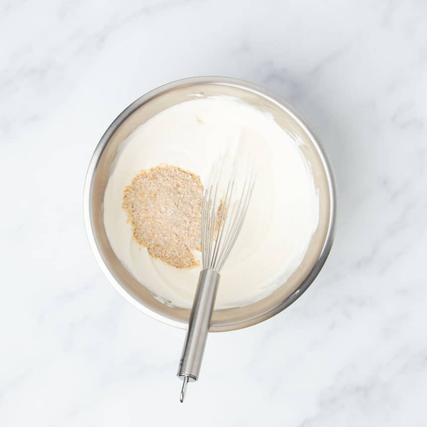 large round metal mixing bowl with whisked white mixture of sour cream and mayonnaise with dry unmixed onion soup mix on top with large wire whisk