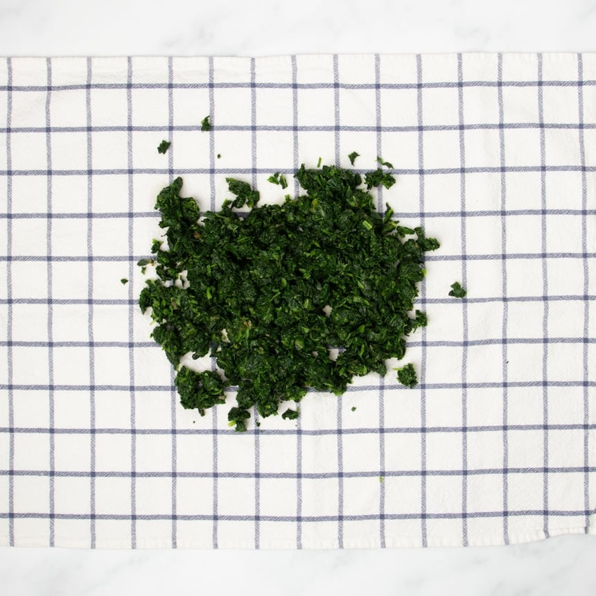 defrosted frozen chopped green spinach on white tea towel with thin blue horizontal and vertical stripes