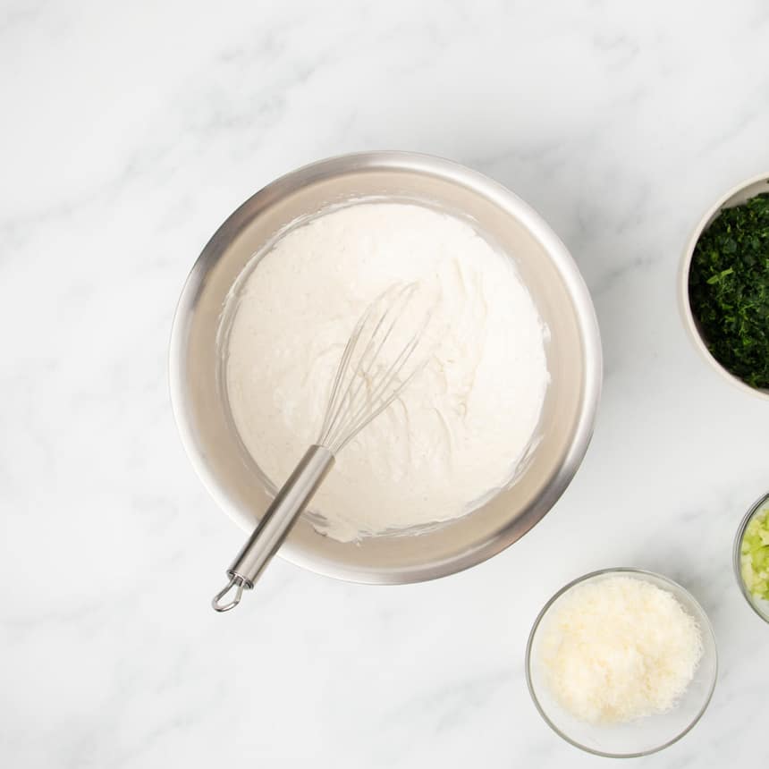 same mixing bowl with ingredients whisked together into soft white mixture with metal wire whisk in bowl