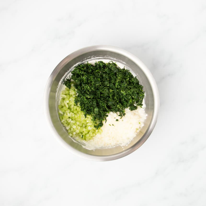 same bowl with white mixture on bottom, minced light green celery, grated white Parmesan cheese and dried chopped spinach on top