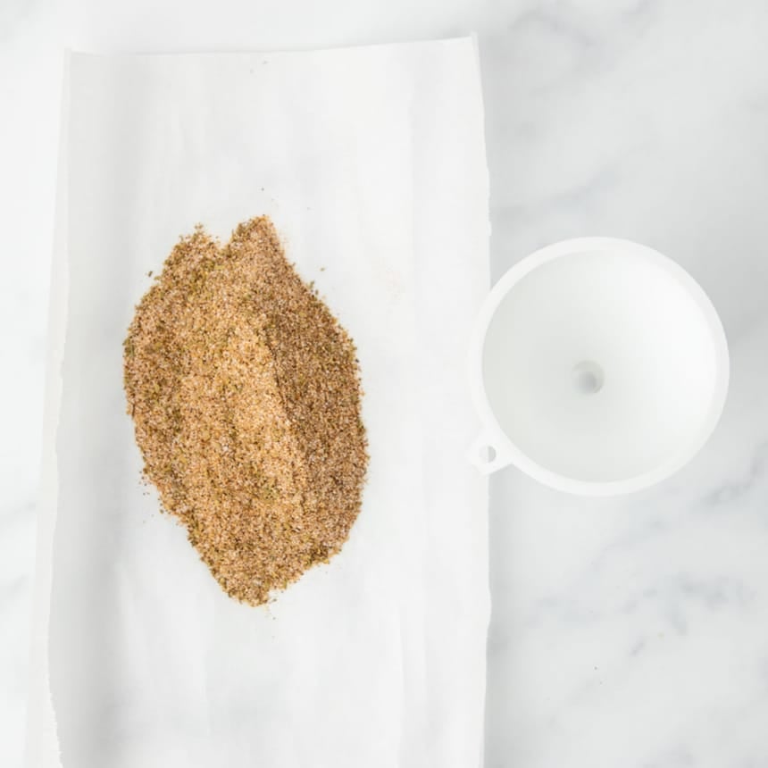 taco seasoning powder on rectangular white parchment next to small white funnel