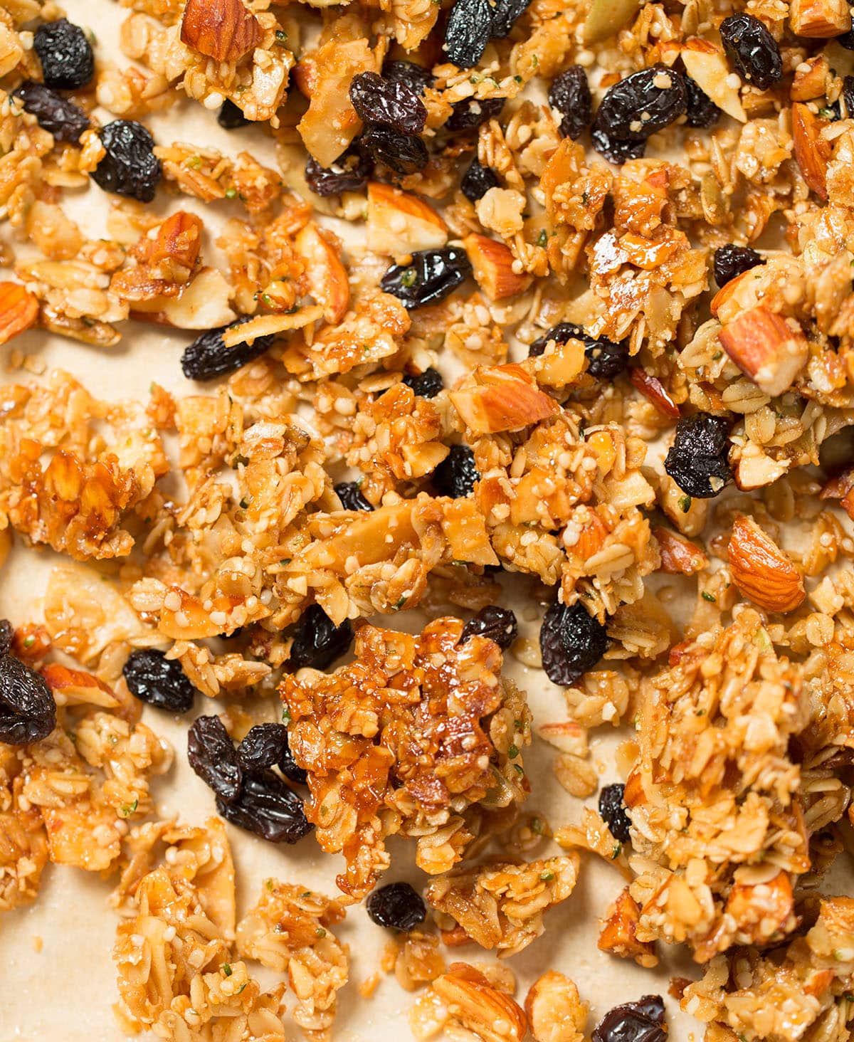 Overhead image of brown clusters of oats, nuts, seeds, and coconut chips on nonstick metal half sheet pan