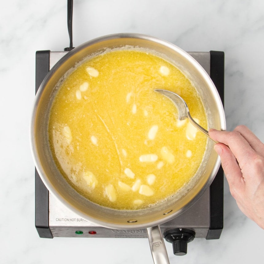 Same mixture in pan with hand holding mixing spoon as ingredients melt, making mixture appear yellow from the melted butter