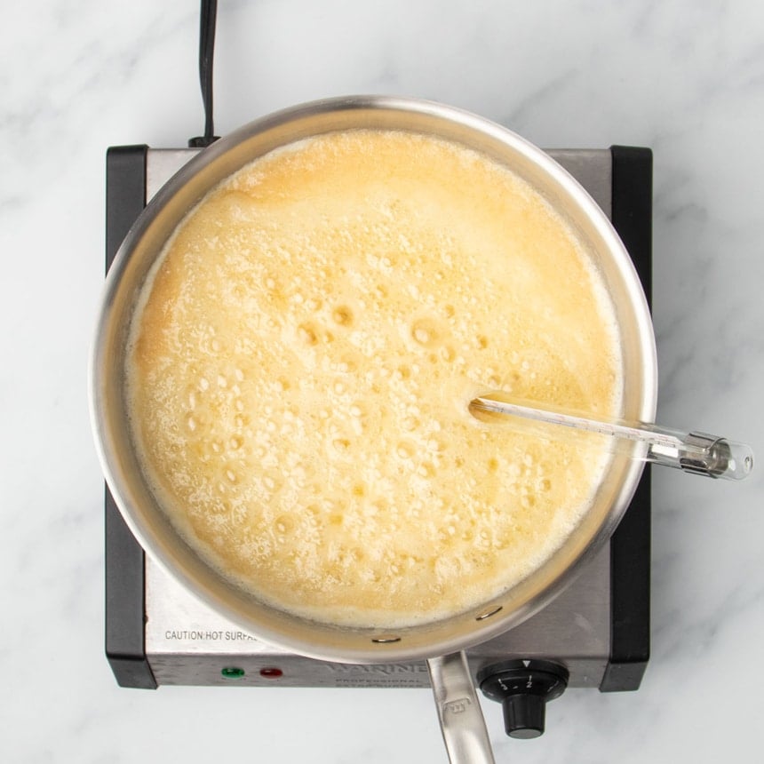 mixture boiling with bubbles and foaming ingredients in same pan, with analog glass candy thermometer attached to side of pan, with end of thermometer in the boiling mixture