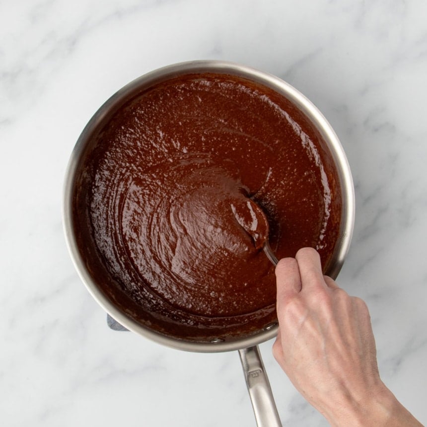 hand holding mixing spoon mixing in chocolate creating a thick, brown swirled liquid mixture